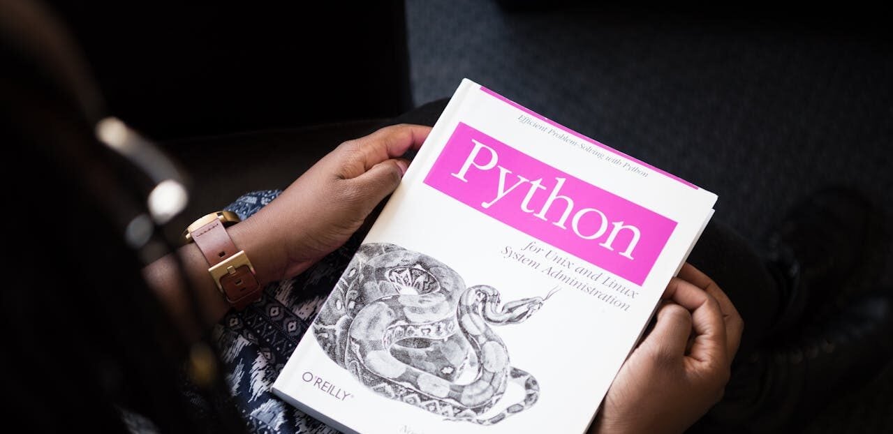 Vista superior de uma pessoa segurando um livro branco e rosa sobre a linguagem de programação Python, com o logo da editora O'Reilly.